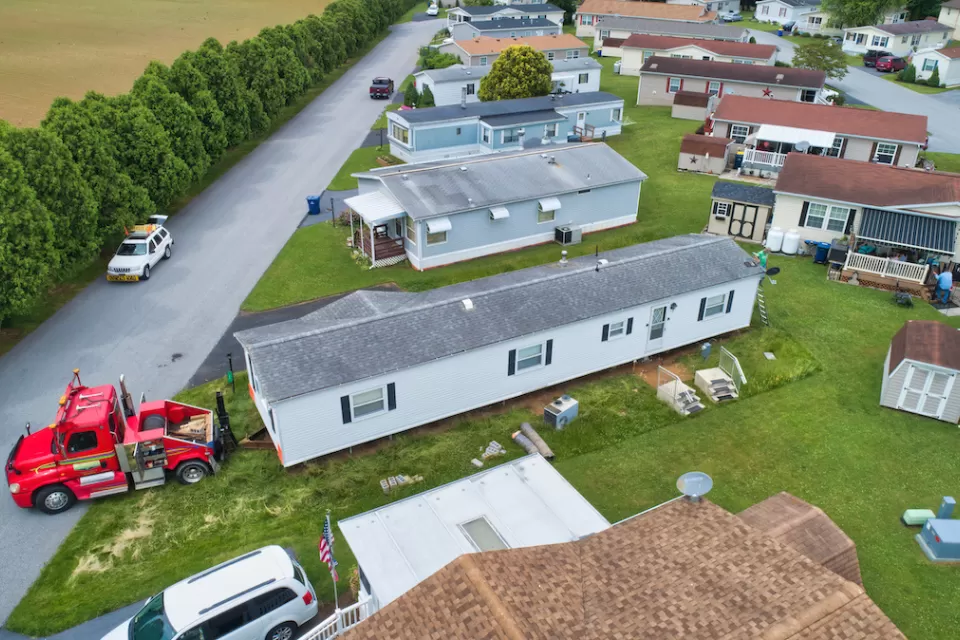 Aerial view of mobile home being moved in a mobile home park by a red truck.